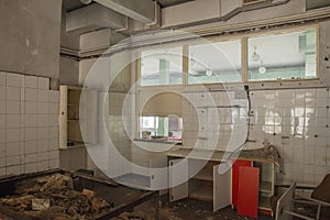 The interior of an abandoned industrial kitchen full of garbage, furniture and glasses left by users. Urbex