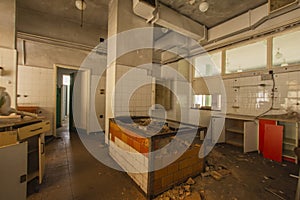 The interior of an abandoned industrial kitchen full of garbage, furniture and glasses left by users. Urbex