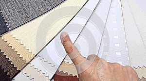 interior architect's hand selects black out drapery samples with different textures in earth color tone, close up view.