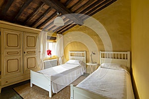 Interior of a bedroom with two single beds. Spartan ambiance and nothing luxurious. The walls are yellow