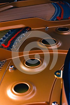 The interior of an black piano with all its details hammers,strings and keys.Golden interior with shades of red