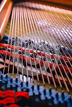 The interior of an black piano with all its details hammers, strings and keys. Golden interior with shades of red