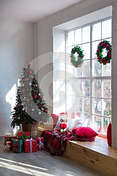 Interior of bright modern living room with big panoramic window decorated with Christmas tree and gifts