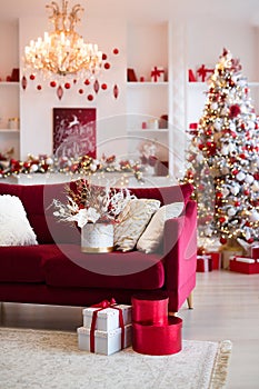 Interior of bright modern living room with fireplace, chandelier and comfortable sofa decorated with Christmas tree and