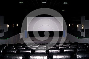 The interior of a cinema hall with black leather seats and a white screen. The film does not show and no people
