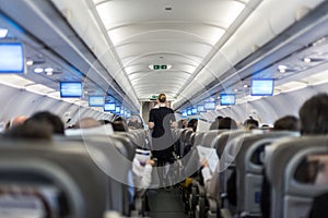 Interior of commercial airplane with stewardess serving passengers on seats during flight. photo