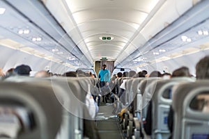 Interior of commercial airplane with stewardess serving passengers on seats during flight.