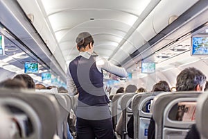 Interior of commercial airplane with stewardess serving passengers on seats during flight.