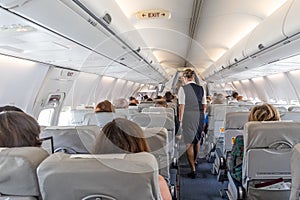 Interior of commercial airplane with stewardess serving passengers on seats during flight.