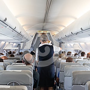 Interior of commercial airplane with stewardess serving passengers on seats during flight.