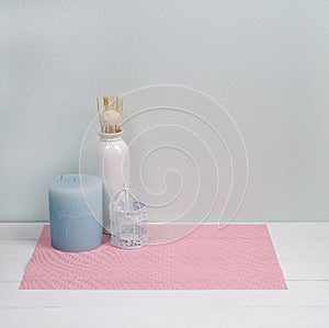 Interior composition of a home, candles, flower, birdcage and vase on pink napkin, white wood background. Modern interior. Minimal