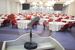 Interior of a conference room. Detail of a microphone sitting on a desk facing the room full of tables and chairs