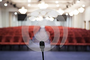 Interior of a conference room. Microphone detail of the speaker facing the room full of red chairs