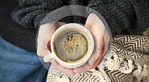 Interior cosy woman hands holding cup of coffee or chocolate with sweater and blanket