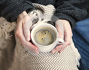 Interior cosy woman hands holding cup of coffee or chocolate with sweater and blanket, comfortable home winter or autumn lifestyle