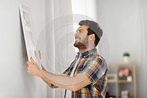 Man hanging picture in frame to wall at home