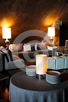 Interior decoration of a restaurant with small tables and lamps and a stack of plates on a table