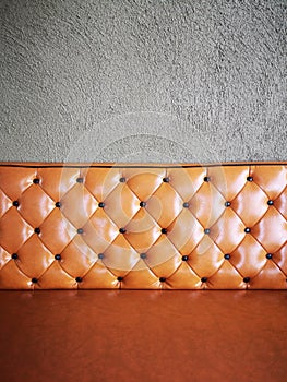 Vintage orange or brick colour leather sofa with grey concrete wall background.