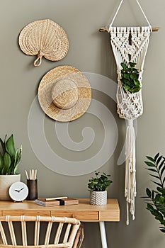 Interior design of boho living room with stylish armchair, wooden desk, house plants, cacti, rattan decoration, macrame.