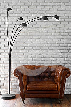 Interior design, a classic brown leather chair against a white brick wall with a modern black lamp with 5 lamps above it