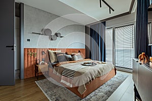 Interior design of elegant bedroom with big orange bed, beige and grey bedclothes, blue curtain, rug, modern lamp, night stand,