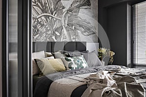 Interior design of harmonized bedroom with beautiful wallpaper, modern bed, flowers in vase, decoration and elegant accessories .