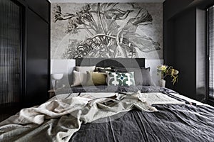 Interior design of harmonized bedroom with beautiful wallpaper, modern bed, flowers in vase, decoration and elegant accessories .