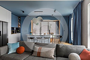 Interior design of kitchen interior with marble kitchen island, black chokers, blue kitchen furnitures, modern lamp, window, gray