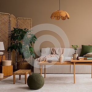 Interior design of living room with modular sofa, wooden coffee table, rattan sideboard, green pillow, lamp, brown pouf, beige