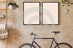 Interior design of living room with two black poster mock up frames, bike and potted plants. Grunge wabi sabi wall.