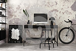 Interior design of loft industrial apartment with black desk, modern black stool, computer screen, vase with dried flowers, lamp,
