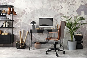 Interior design of office interior with black desk, modern dark armchair, computer screen, black lamp, simple rack, gray flower