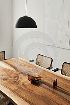 Interior design of stylish dining room interior with family wooden table, modern chairs, plate with nuts, salt and pepper shakers.