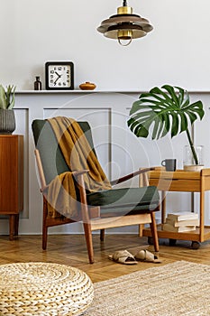 Interior design of stylish living room with vintage green armchair, coffee table, furniture, grey wall, shelf, carpet, plants.