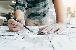 Interior designer or architect reviewing blueprints and holding pencil drawing on desk at home office