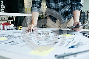 Interior designer or architect reviewing blueprints and holding pencil drawing on desk at home office