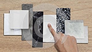 interior designer's hand selects premium stone samples including black marble, grey artificial stone, terrazzo tiles.