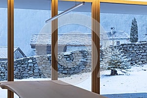 Interior of a dining room, with a large bay window, no one inside and outside there is snow