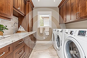 Interior of elegant laundry room in a modern house. Wooden cabinets, marble tabletop with built-in sink, washing machine