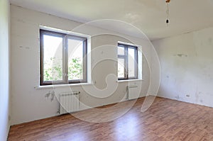 The interior of an empty room during renovation, there are two large windows in the room, radiators under them