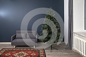 Interior with gray seventies style sofa, carpet and Christmas tree with cones in an empty room with blue walls