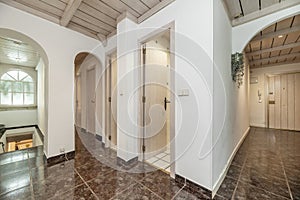 Interior hallways of a house with dark stoneware floors and different light wooden doors