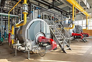 The interior of an industrial boiler room with three large boilers, many pipes, valves and sensors