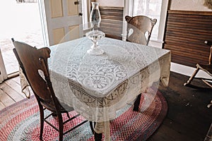 Interior of a kitchen, with antique table, lace tablecloth, and a hurricane lamp