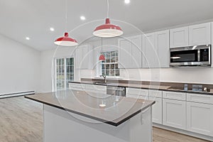 Interior of a kitchen with white cabinets, red hanging lamps, a counter and a parquet floor