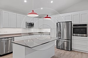 Interior of a kitchen with white cabinets, red hanging lamps, a parquet floor, electrical appliances