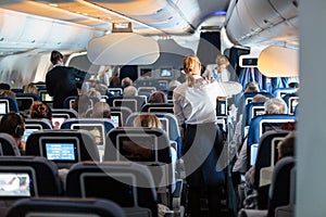 Interior of large commercial airplane with stewardesses serving passengers on seats during flight.