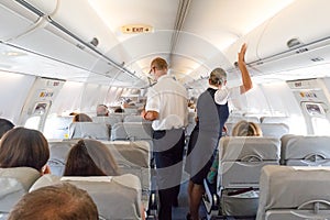 Interior of large commercial airplane with stewardesses serving passengers on seats during flight.