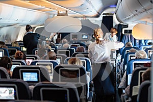 Interior of large commercial airplane with stewardesses serving passengers on seats during flight.