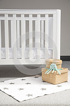 Interior of light baby room with a modern cozy crib and woven wicker boxes on a soft starry carpet